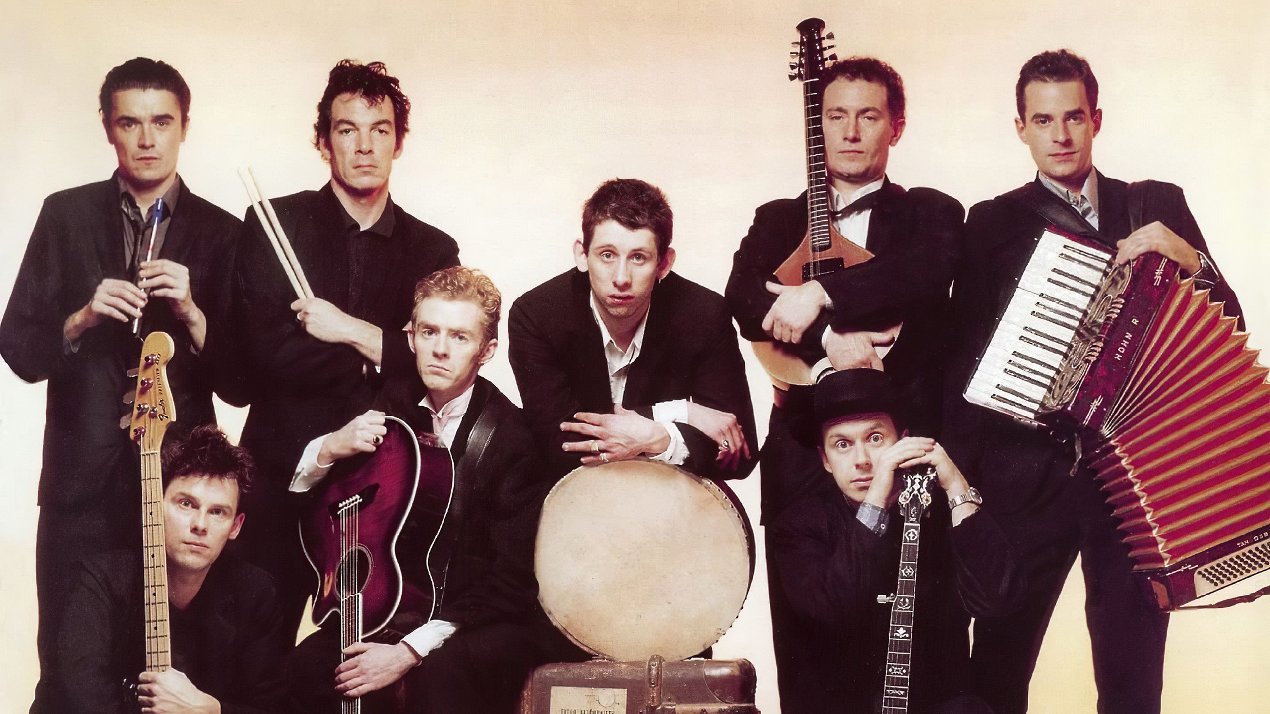 A picture of the Pogues: 8 men in old-fashioned suits, holding their instruments, sat on battered steamer trunks and suitcases, looking awkward and serious against a faded, yellowing background.